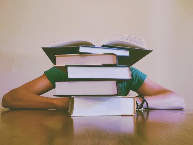 student with head down before stack of books